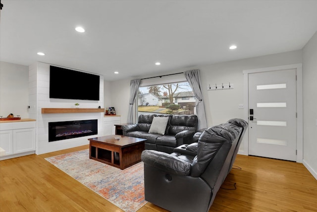 living room featuring recessed lighting, a glass covered fireplace, and light wood finished floors