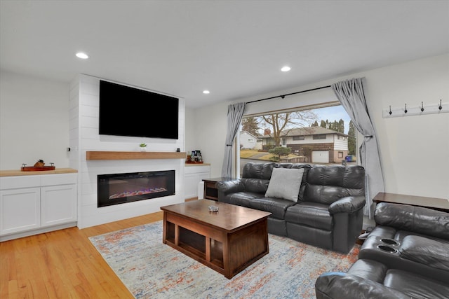 living area featuring light wood finished floors, a glass covered fireplace, and recessed lighting