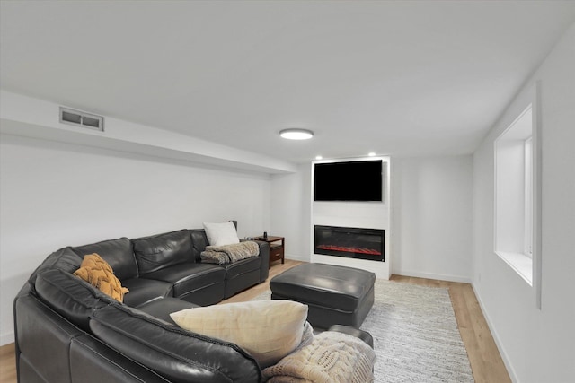 living area with visible vents, light wood-style flooring, baseboards, and a glass covered fireplace