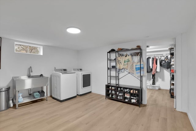 laundry area with baseboards, washer and clothes dryer, laundry area, wood finished floors, and a sink