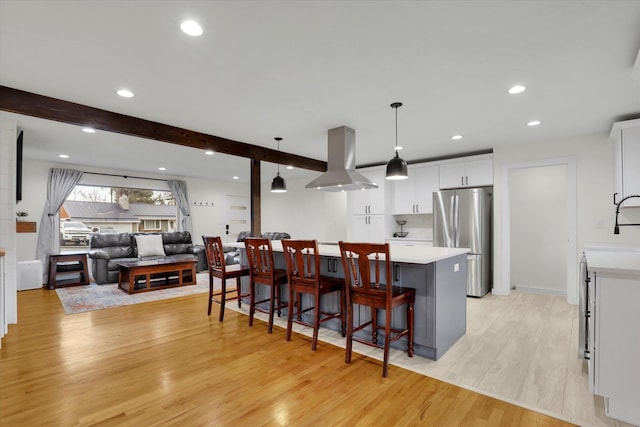 kitchen with beam ceiling, island exhaust hood, freestanding refrigerator, light wood finished floors, and light countertops