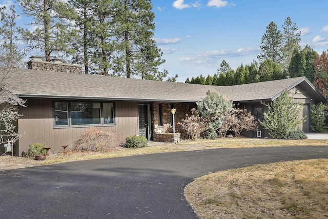 ranch-style home with a garage, roof with shingles, a chimney, and driveway