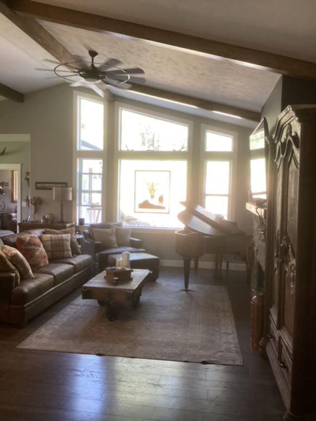 living area with lofted ceiling with beams, a ceiling fan, and dark wood-style flooring