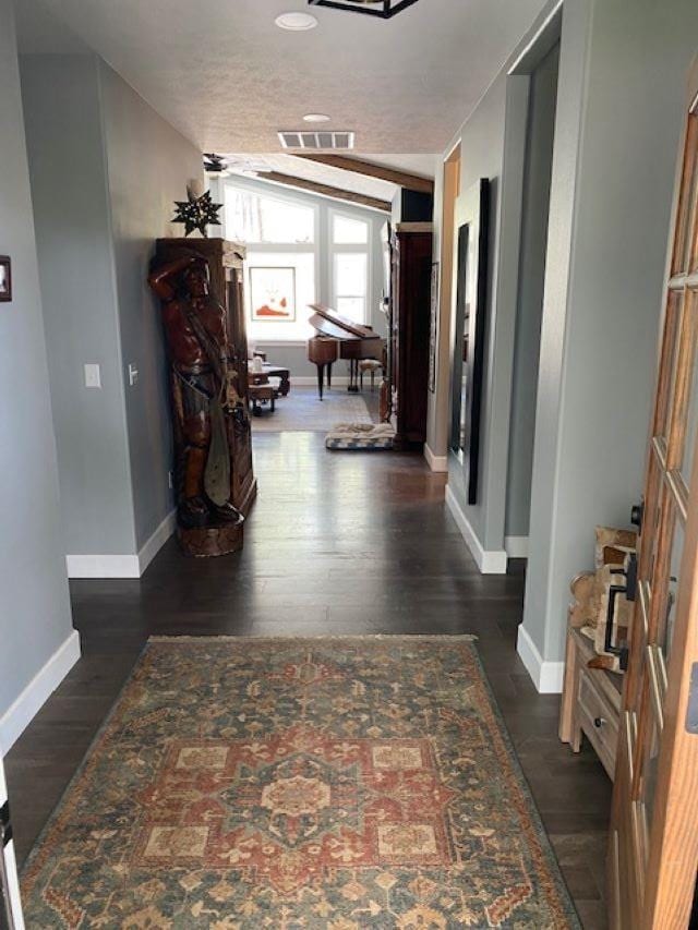 hall with dark wood-style floors, visible vents, and baseboards