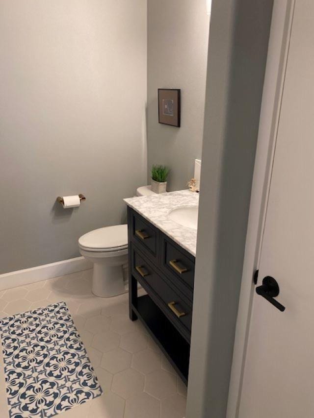 half bath with baseboards, toilet, and vanity