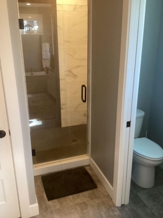 bathroom with toilet, baseboards, and a stall shower