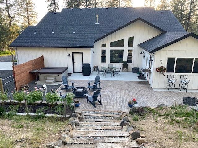 rear view of property with a hot tub, a fire pit, a patio, and roof with shingles