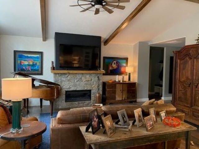 living area with lofted ceiling with beams, a stone fireplace, and ceiling fan