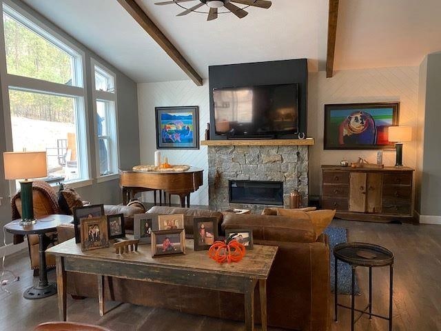 living room featuring ceiling fan, baseboards, lofted ceiling with beams, a fireplace, and wood finished floors