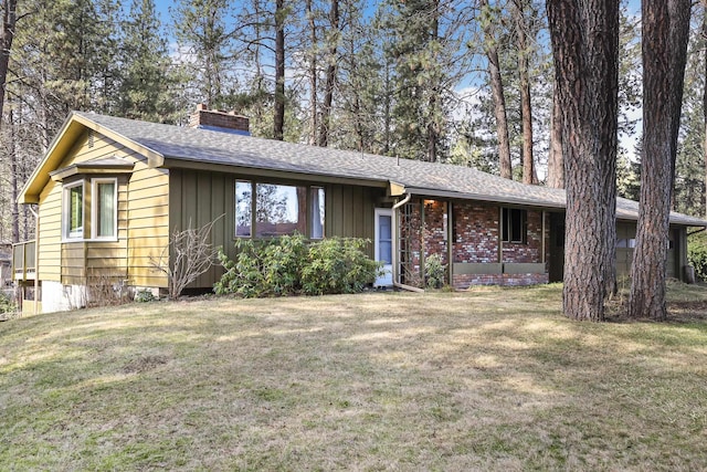 ranch-style home featuring brick siding, board and batten siding, a shingled roof, a front yard, and a chimney