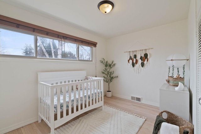 bedroom featuring a nursery area, wood finished floors, visible vents, and baseboards