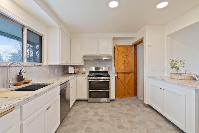 kitchen with a sink, decorative backsplash, under cabinet range hood, appliances with stainless steel finishes, and white cabinetry