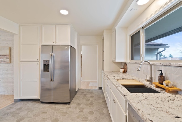 kitchen featuring white cabinets, light stone counters, stainless steel fridge, and a sink