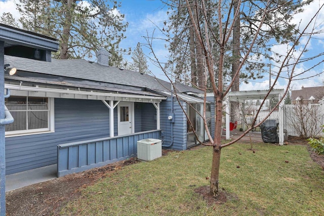 exterior space with a shingled roof, a yard, and fence