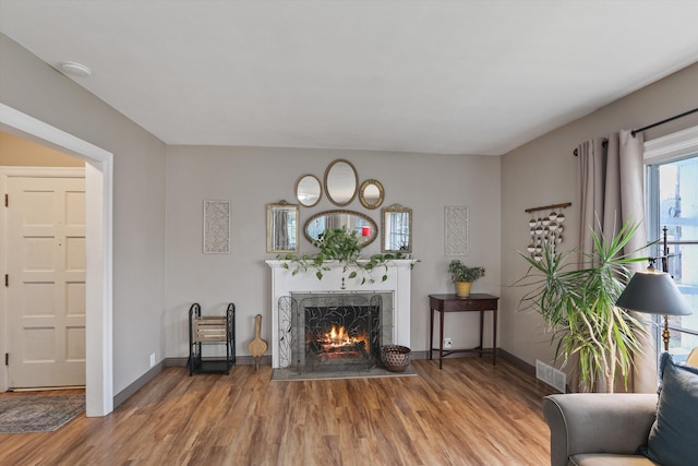 living area with visible vents, baseboards, a lit fireplace, and wood finished floors