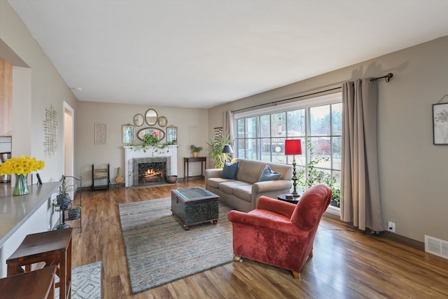 living room featuring a premium fireplace, visible vents, baseboards, and wood finished floors