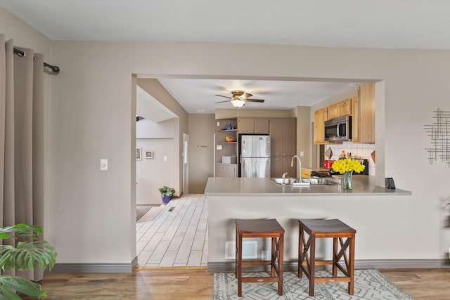 kitchen featuring a peninsula, stainless steel appliances, light wood-style floors, and a sink