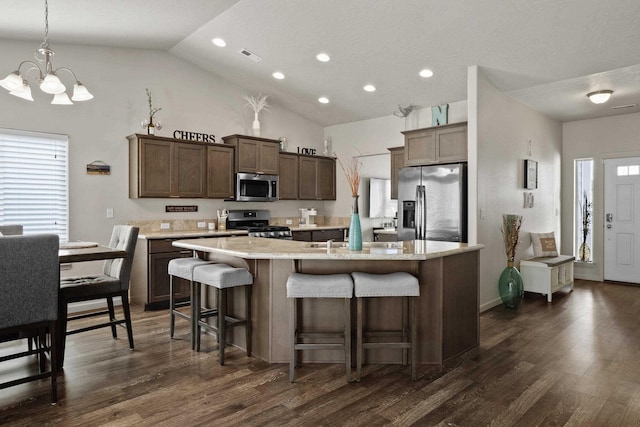 kitchen with a kitchen bar, an island with sink, dark wood-style floors, and appliances with stainless steel finishes