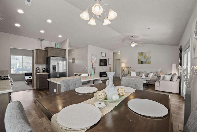 dining area featuring ceiling fan with notable chandelier, vaulted ceiling, visible vents, and dark wood-style flooring