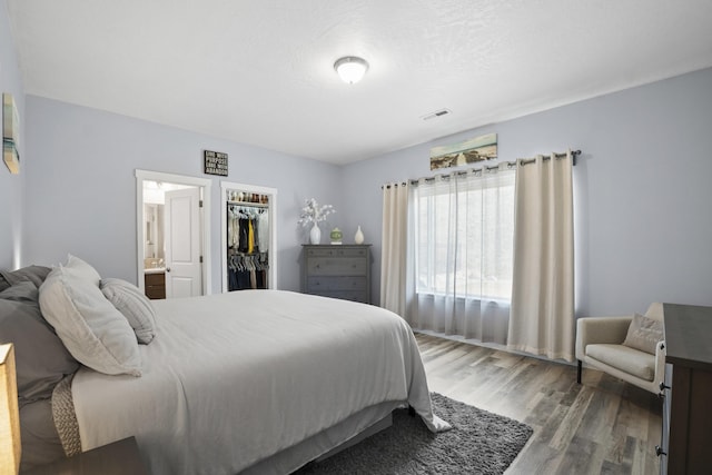 bedroom with visible vents, a walk in closet, ensuite bathroom, wood finished floors, and a closet