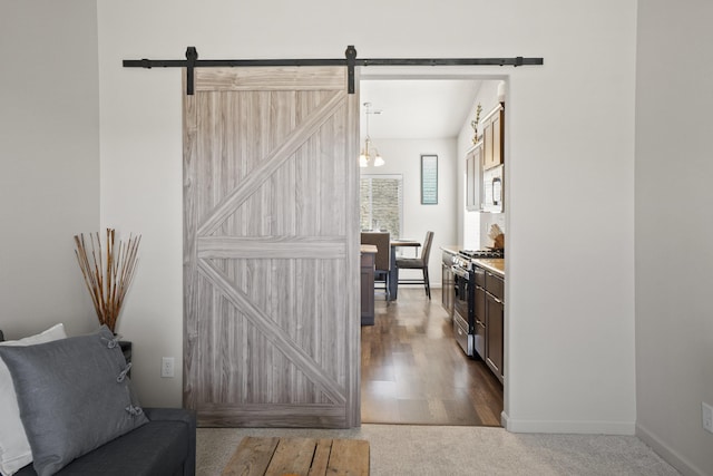 hallway featuring a barn door, baseboards, carpet, and wood finished floors