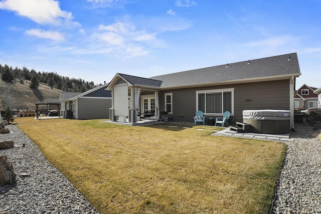 back of property with a lawn, a hot tub, a patio, and a shingled roof