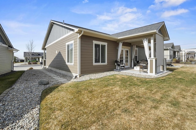 back of house with board and batten siding, fence, a lawn, french doors, and a patio