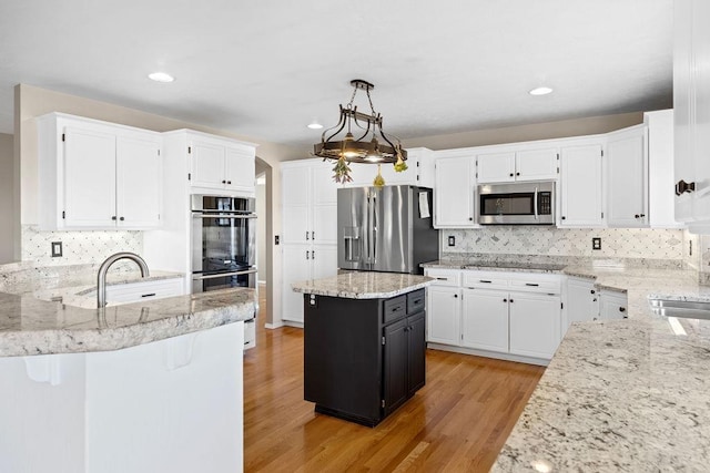 kitchen with light stone countertops, light wood-style flooring, appliances with stainless steel finishes, white cabinets, and a sink