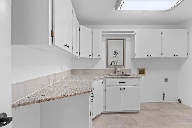 kitchen featuring light stone counters, white cabinetry, and a sink