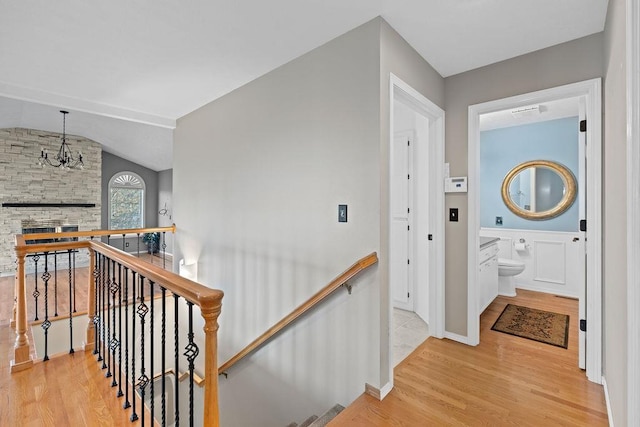 corridor with an upstairs landing, lofted ceiling, and wood finished floors