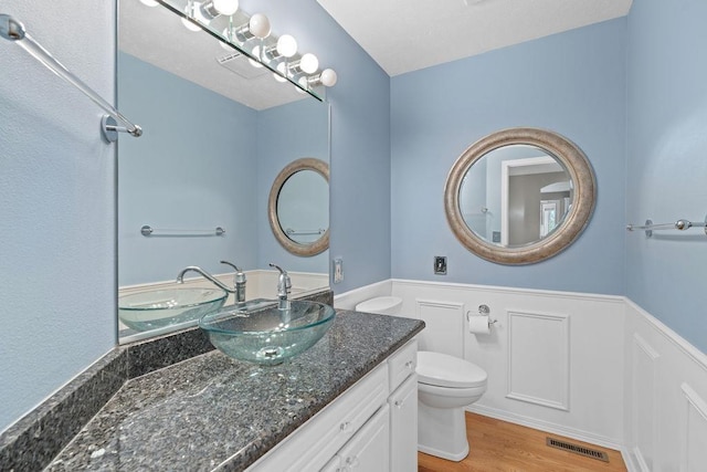 bathroom with visible vents, toilet, wood finished floors, wainscoting, and vanity