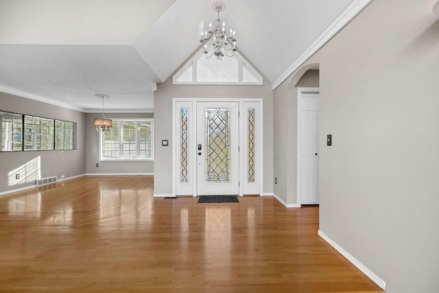 entrance foyer featuring visible vents, wood finished floors, arched walkways, an inviting chandelier, and baseboards