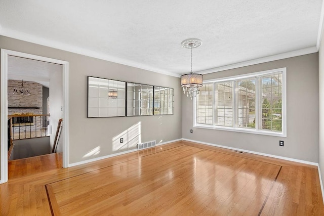 unfurnished dining area featuring visible vents, baseboards, a fireplace, an inviting chandelier, and wood finished floors