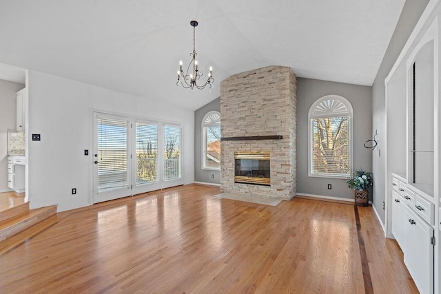 unfurnished living room featuring baseboards, lofted ceiling, light wood-style flooring, a fireplace, and an inviting chandelier