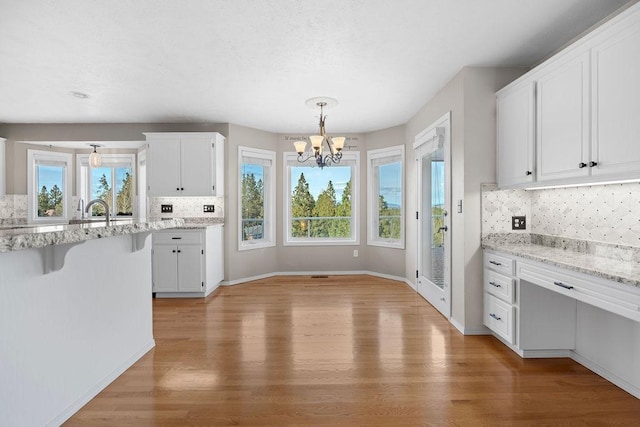 kitchen with decorative backsplash, an inviting chandelier, white cabinets, and light wood-type flooring