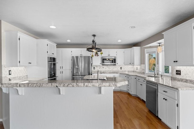 kitchen featuring light wood-style flooring, a sink, stainless steel appliances, a peninsula, and light stone countertops