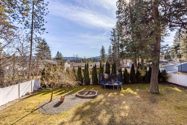 view of yard with a trampoline, a fenced backyard, and an outdoor fire pit