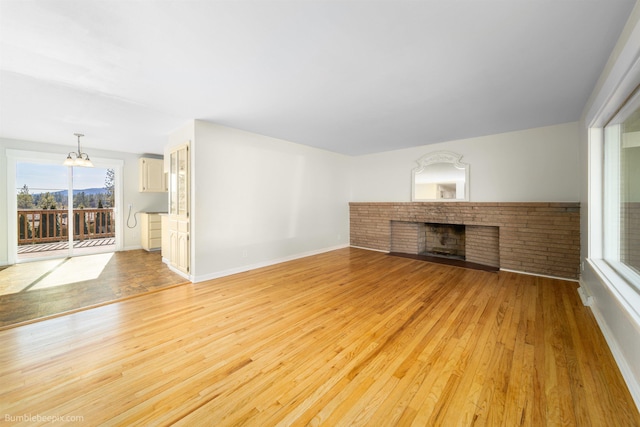 unfurnished living room featuring light wood-style flooring, a brick fireplace, and baseboards