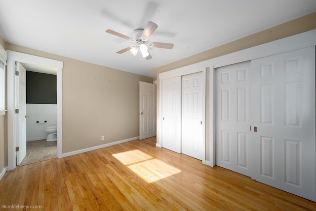 unfurnished bedroom with wainscoting, ensuite bathroom, two closets, and light wood-type flooring