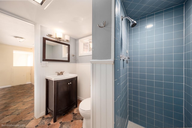 full bath featuring vanity, plenty of natural light, a tile shower, wainscoting, and toilet