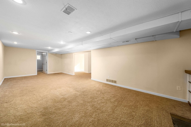 basement featuring visible vents, baseboards, light colored carpet, and a textured ceiling