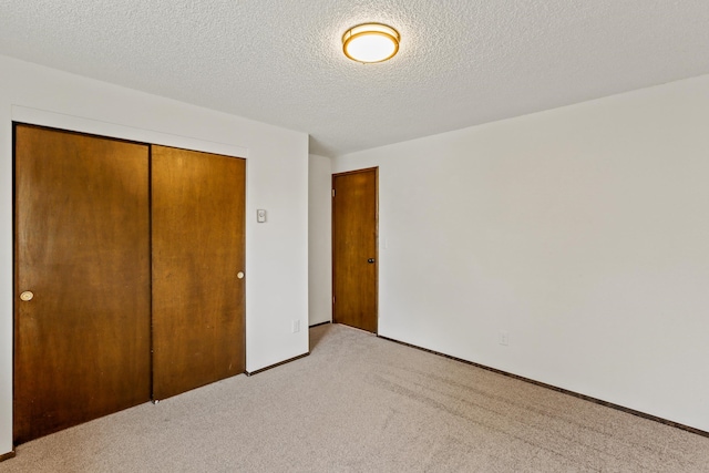 unfurnished bedroom featuring light carpet, baseboards, a textured ceiling, and a closet