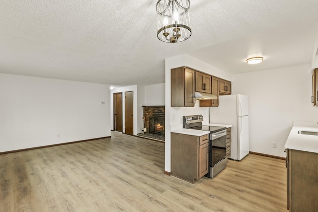 kitchen featuring light wood finished floors, light countertops, stainless steel range with electric stovetop, under cabinet range hood, and a brick fireplace