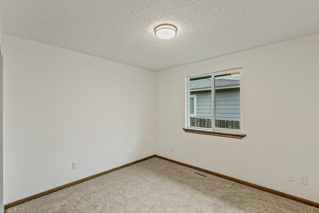 carpeted spare room featuring baseboards, visible vents, and a textured ceiling