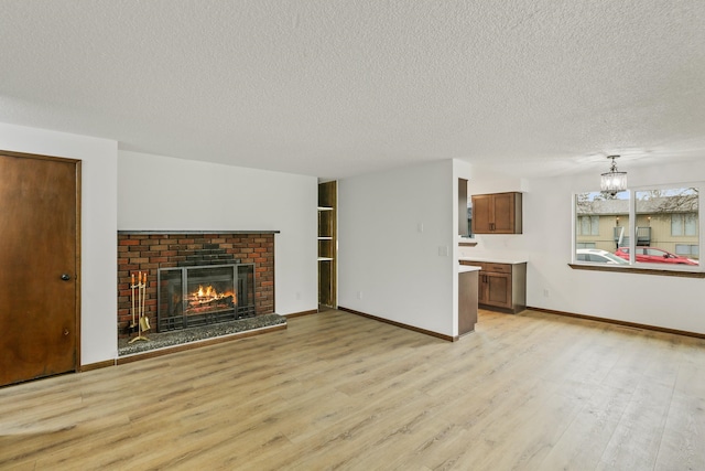 unfurnished living room featuring a brick fireplace, light wood-style flooring, baseboards, and a textured ceiling