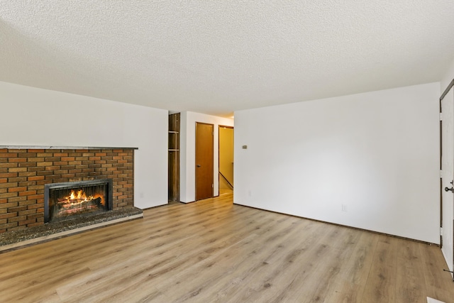 unfurnished living room with light wood finished floors, a brick fireplace, and a textured ceiling