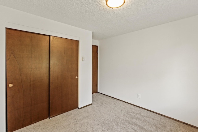 unfurnished bedroom with a closet, a textured ceiling, light carpet, and baseboards