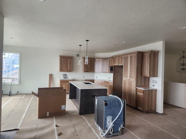 kitchen featuring a textured ceiling, stainless steel microwave, brown cabinetry, and a kitchen island