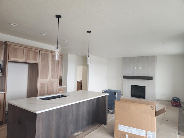 kitchen featuring light stone counters, a fireplace, a textured ceiling, decorative light fixtures, and a center island