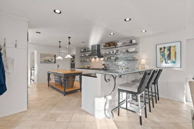 kitchen with a breakfast bar, open shelves, a peninsula, wall chimney exhaust hood, and decorative backsplash